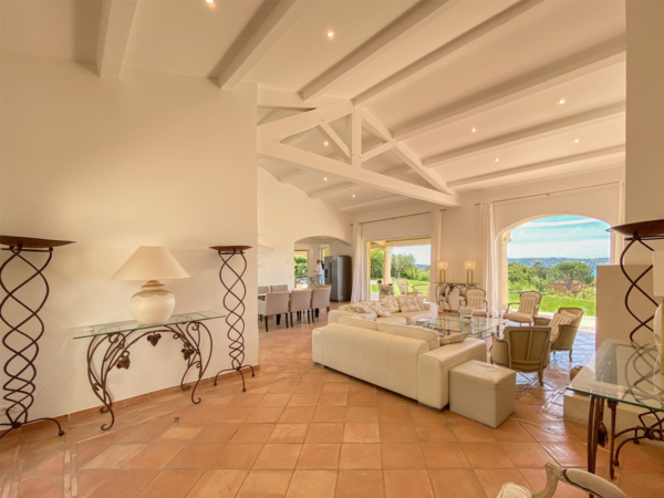 Expansive Mediterranean living room featuring terracotta tiled floors, multiple white leather sofas, ornate wrought iron lamps, and large arched doorways leading to a lush garden and ocean view. Immerse yourself in the expansive and airy ambiance of this Mediterranean-style living room, captured in a luxurious villa. This image showcases a spacious layout with terracotta tiled floors that echo the warmth of the natural surroundings. White leather sofas are strategically arranged to foster a welcoming conversation area, while ornate wrought iron floor lamps provide both illumination and a decorative touch. The room's large arched doorways open up to a captivating garden and distant ocean views, seamlessly blending indoor comfort with the beauty of the outdoors. This living space is perfect for those looking to draw inspiration for creating a luxurious yet comfortable home environment that harmonizes with natural elements.