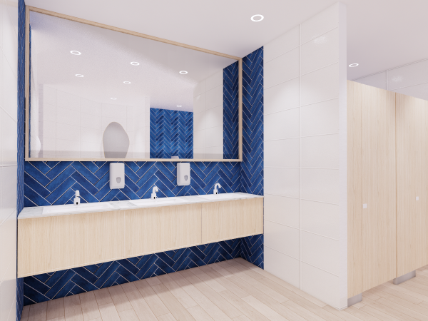Interior of a men’s washroom with a large mirror, white sinks on a wooden vanity against a herringbone-patterned blue accent wall, and wood-paneled stall doors. The design of this men's washroom marries functionality with contemporary style. A spacious mirror runs the length of the room, reflecting the streamlined white sinks mounted on a wooden vanity, which introduces a touch of natural warmth to the space. Below the mirror, the eye-catching blue tiles arranged in a herringbone pattern add a splash of dynamic color and texture, contrasting with the clean lines of the white wall tiles. Privacy is afforded by wood-paneled stall doors, enhancing the room's modern yet welcoming ambiance. Bright, well-placed lighting ensures the space is both inviting and practical, ideal for a high-end commercial or hospitality setting.