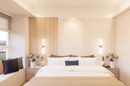 Modern bedroom with a wooden accent wall, plush bedding, and elegant bedside decor. This modern bedroom epitomizes tranquil minimalism, anchored by a spacious bed with crisp white linens and a beige comforter against a rich wooden accent wall that introduces a natural element. Navy and brown textured pillows provide a cozy contrast, while the wall-mounted brass lights cast a warm ambiance over the decor, including bedside vases of delicate pink roses, books, and tasteful ornaments. The room's neutral tones are complemented by white paneled walls and soft cove lighting above, with a window allowing filtered natural light to enhance the space's calm and inviting feel.