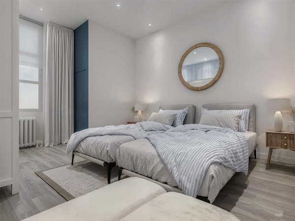 A spacious bedroom with two twin beds, a round mirror, and a blue accent wall.