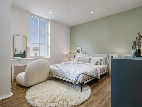 A modern bedroom with a large window, a green accent wall, a white bed, and a round rug.