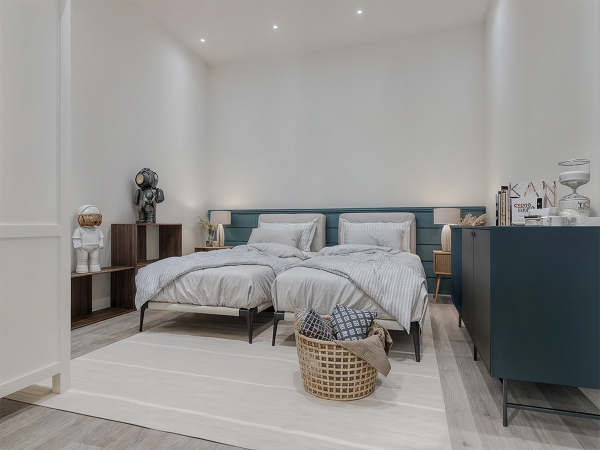 A minimalist bedroom with two twin beds, a blue dresser, and a white rug.