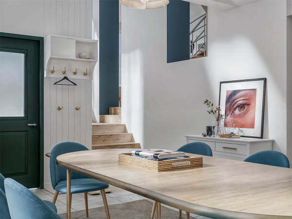 A modern dining room with a blue accent wall, a wooden dining table, and blue velvet chairs.