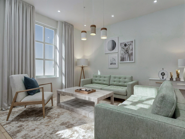 A modern living room with a large window, a white coffee table, two green sofas, and a patterned rug.